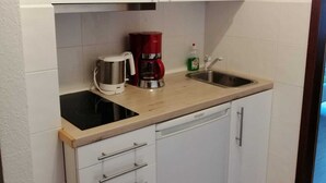 Cocina compacta con alacenas blancas, un lavamanos, cafetera y lavavajillas.