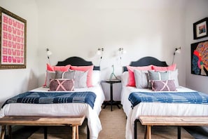 A room with two beds, each with a black headboard and multiple pillows. There is a small table between the beds, and a lamp on the wall. - Getaway Minutes from RT Square | Sunset Views (Burton)