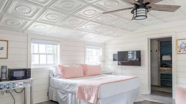 Un dormitorio con cama, ventilador de techo, televisor y ventana.
