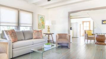A spacious living room with a sofa, armchairs, a glass coffee table, and a ceiling fan.