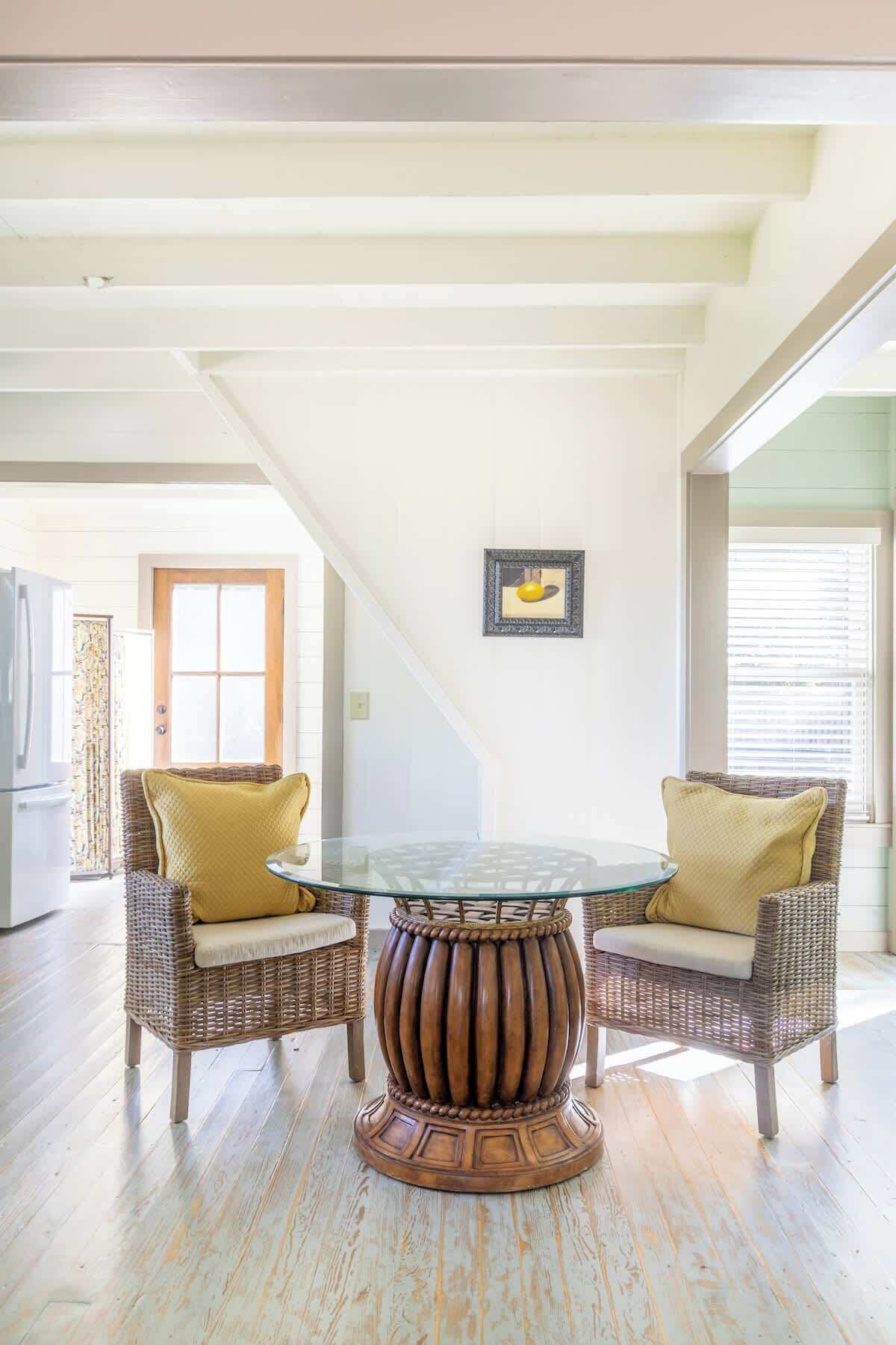 A dining area with wicker chairs, a glass table, and a wooden base.