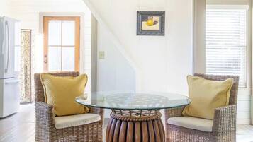 A dining area with wicker chairs, a glass table, and a wooden base.