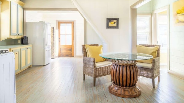 A spacious kitchen with wooden flooring, a dining area with wicker chairs and a glass table, and a large window providing natural light. - Walk to Round Top Restaurants+Bars+Shops | Meme (Round Top)