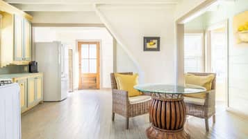 A spacious kitchen with wooden flooring, a dining area with wicker chairs and a glass table, and a large window providing natural light.