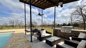 An outdoor patio with stone flooring, wicker furniture, a grill, and a pool.