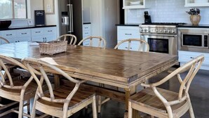 A modern kitchen with white cabinetry, a wooden dining table, and wicker chairs.