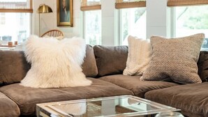 A living room with a brown sofa, white fluffy pillows, a glass coffee table, and a framed picture on the wall. - Pool + 2 homes + Sleeps 10 | 6 Min. to Round Top (Round Top)