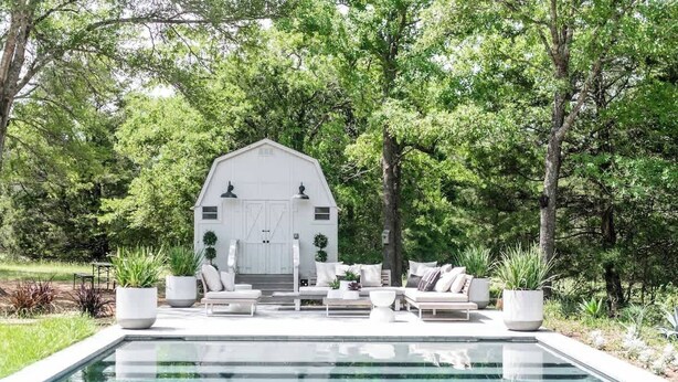 A pool area with a white barn-like structure, surrounded by lush greenery. - Pool + 2 homes + Sleeps 10 | 6 Min. to Round Top (Round Top)