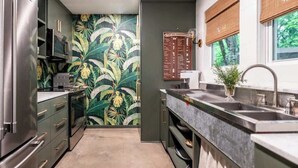 A compact kitchen with a modern stainless steel refrigerator, microwave, and oven. A large window with a view of greenery is visible, and a decorative plant is placed on the counter. - Pool + 2 homes + Sleeps 10 | 6 Min. to Round Top (Round Top)