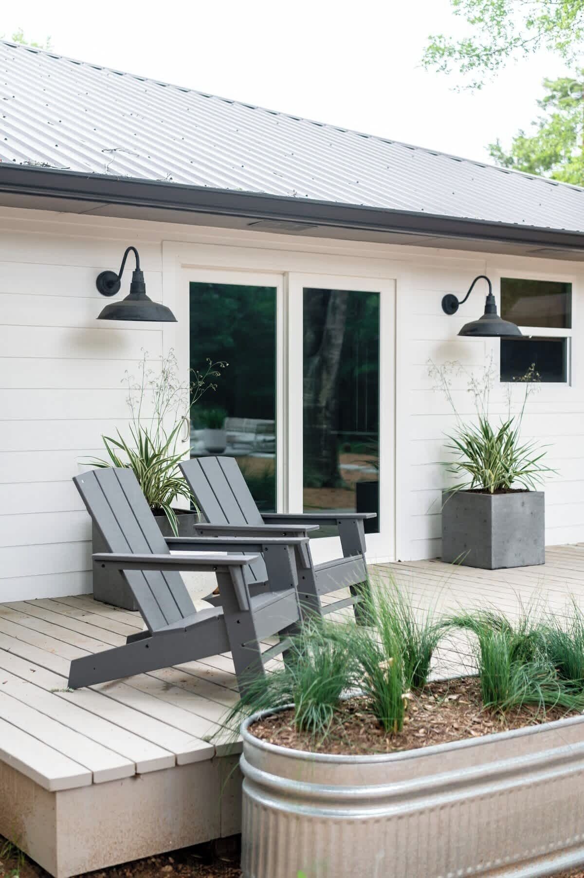 Ein modernes Haus mit einer Holzterrasse, zwei Adirondack-Stühlen und Kübelpflanzen.