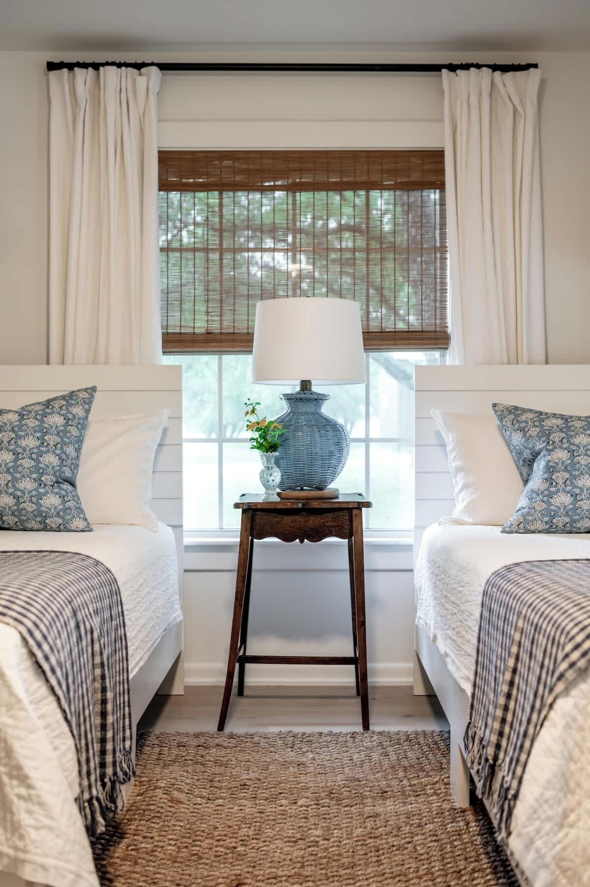 Un dormitorio con dos camas, una mesita de noche con lámpara y una ventana con persianas.