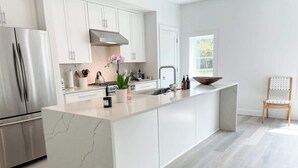 A modern kitchen with white cabinetry, a marble island, stainless steel appliances, and a wooden chair.