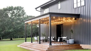 A modern house with a covered outdoor area featuring a wooden deck, outdoor seating, and string lights.