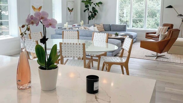 A modern living room with a round dining table, a sofa, and a coffee table. There are hanging pendant lights, a potted plant, and a floor lamp.