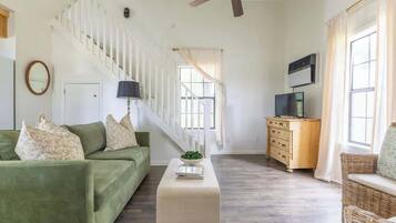 A spacious living room with a green sofa, a white coffee table, a wooden dresser, and a staircase.