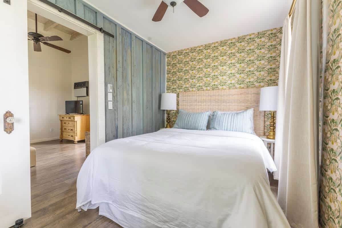 A bedroom with a bed, two bedside lamps, a ceiling fan, and a dresser.