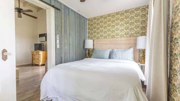 A bedroom with a bed, two bedside lamps, a ceiling fan, and a dresser.