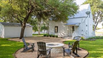 A white house with a fire pit and Adirondack chairs in the yard.