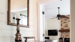 Een woonkamer met houten vloer, een open haard, een aan de muur bevestigde televisie en een plafondventilator.