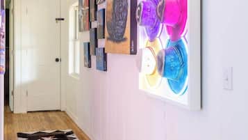 A hallway with a wooden floor, white walls, and a series of artworks including a neon-lit sculpture.