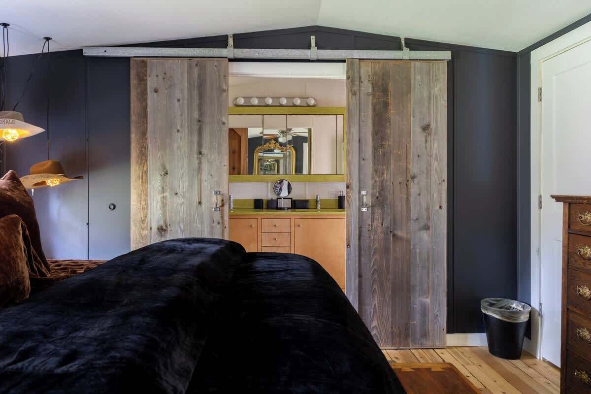 Une chambre avec un lit noir, une armoire en bois et un coin cuisine visible à travers une porte coulissante.