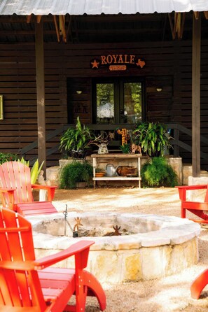 A wooden building with a sign reading 'ROYALE ROUND TOP TEXAS' and a covered outdoor seating area with red chairs and a fire pit. - Western Lifestyle Meets Round Top | Royale #1 (Ledbetter)
