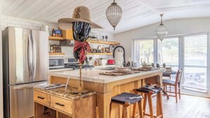 Una cocina moderna con una isla grande, taburetes de madera, electrodomésticos de acero inoxidable e iluminación colgante.