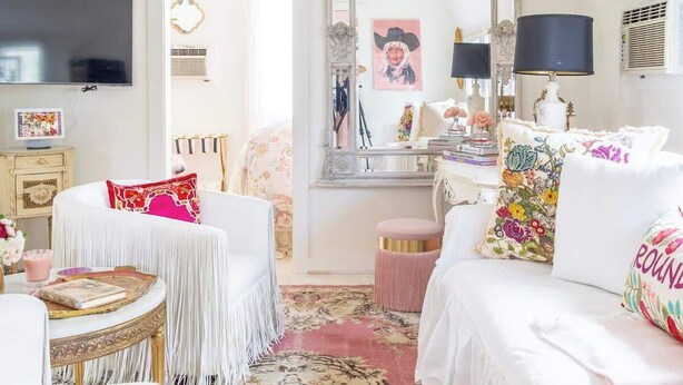 A room with a white bed, a round table, a mirror, and a television. - Wine, Dine, & Unwind | Stay in Style + Shop RT (Carmine)