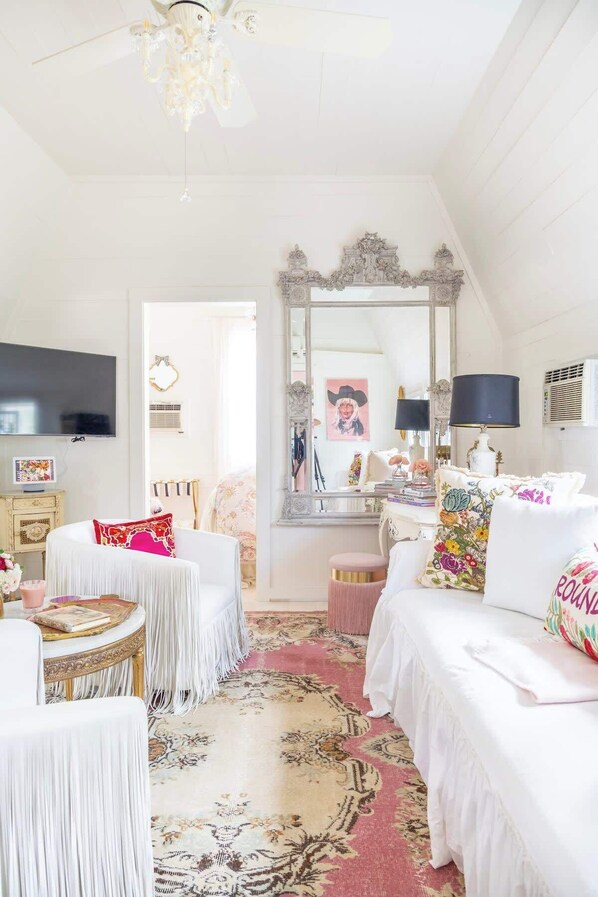 A room with a white bed, a round table, a mirror, and a television.