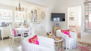 A spacious living room with a white sofa set, a chandelier, a flat-screen TV, and a dining area with a white table and chairs. - Wine, Dine, & Unwind | Stay in Style + Shop RT (Carmine)