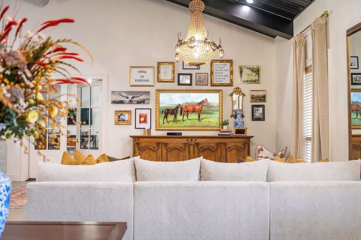 A living room with a large sofa, a chandelier, and a wall decorated with framed pictures and a television.