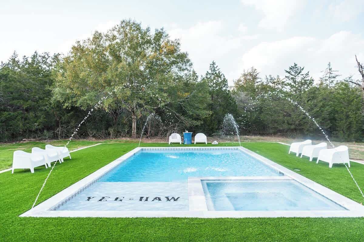A rectangular pool with a clear blue water surface, surrounded by a well-maintained lawn and white lounge chairs.