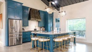 Una cocina moderna con armarios azules, un refrigerador de acero inoxidable, una isla grande con taburetes y una araña.