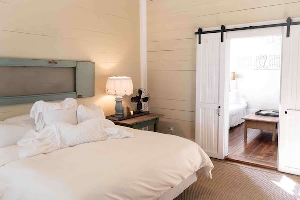 A bedroom with a bed, a nightstand with a lamp, a sliding door to a balcony, and a wooden floor.
