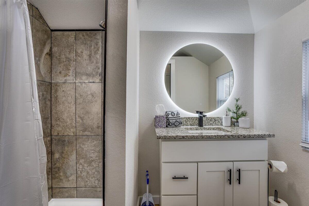 A bathroom with a shower, a sink with a large mirror, and a toilet.
