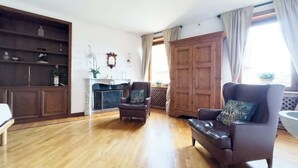 A spacious living room with wooden flooring, a fireplace, a large wooden cabinet, and a comfortable seating area with a sofa and armchair. - Maison Giulia (Rome)