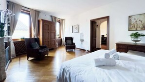 A hotel room with a large bed, two armchairs, a wooden wardrobe, and a desk with a plant. - Maison Giulia (Rome)