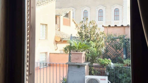 A view from a window overlooking a building with a tiled roof and multiple windows. There is a potted plant in the foreground. - Maison Giulia (Rome)