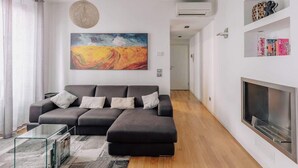 Una sala de estar moderna con un sofá seccional, una mesa de centro de vidrio, una chimenea y un cuadro grande en la pared.