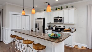 A kitchen with white cabinets, a granite countertop, a stainless steel refrigerator, a microwave, and a coffee maker. There are three wooden bar stools and a bowl of fruit on the counter. - Wilmington's Heart, Pet-Friendly, Comfy Beds, Kids room! (Wilmington)
