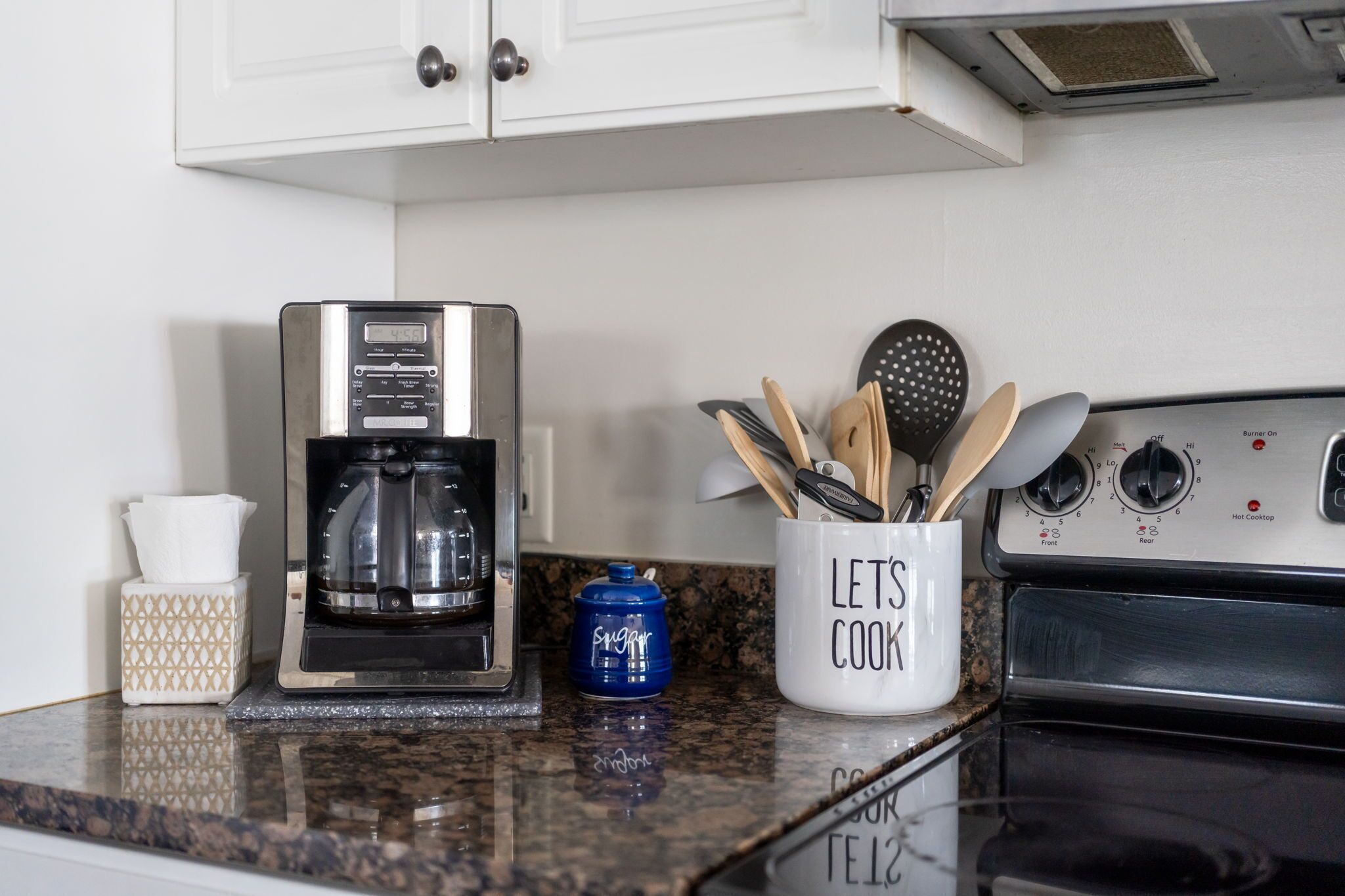 A kitchen counter with a coffee maker, a spice jar, and a mug with utensils.