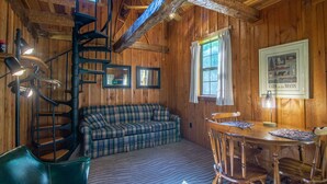 A cozy cabin interior with a plaid sofa, a wooden dining table with chairs, a spiral staircase, and framed pictures on the walls. - Moore House Inn & Cabins (Marlinton)