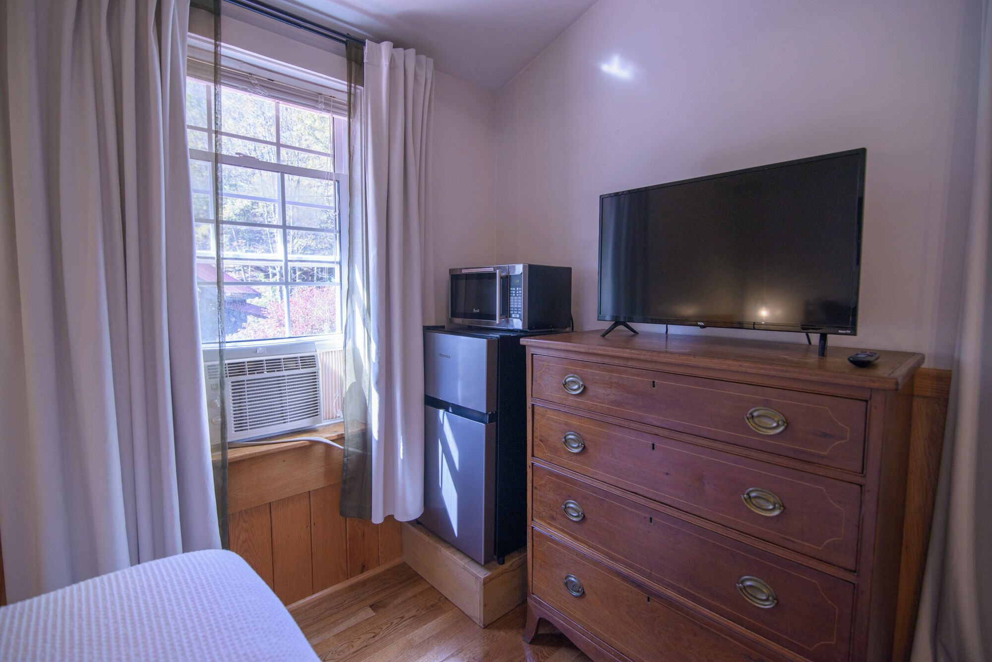 Una habitación pequeña con un aparador de madera, un televisor, un microondas y un refrigerador.