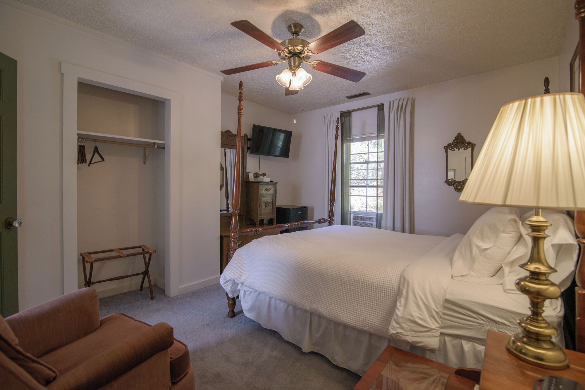 A bedroom with a bed, a ceiling fan, a TV, a dresser, and a chair.
