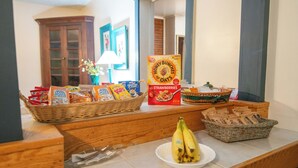 A breakfast buffet with various cereals, a basket of bananas, and a wicker basket with bread. - Moore House Inn & Cabins (Marlinton)