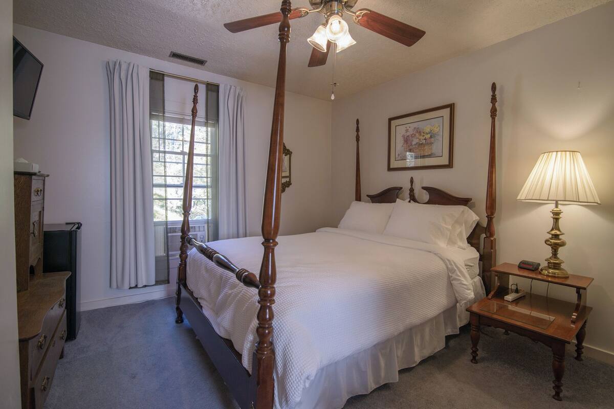 A four-poster bed with a wooden frame, a bedside table with a lamp, and a painting on the wall.