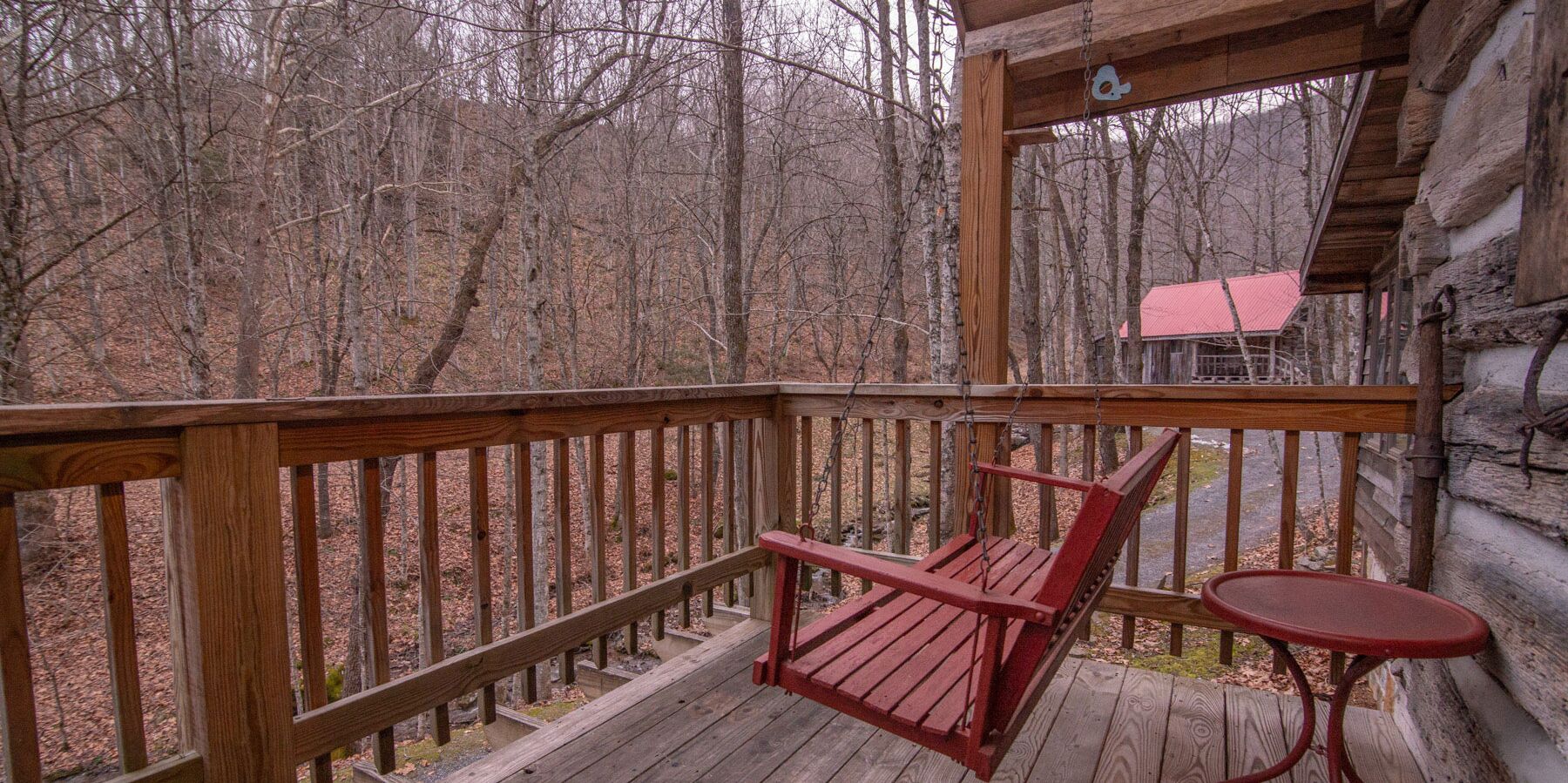 Une terrasse en bois avec une chaise rouge et une petite table, donnant sur une zone boisée.
