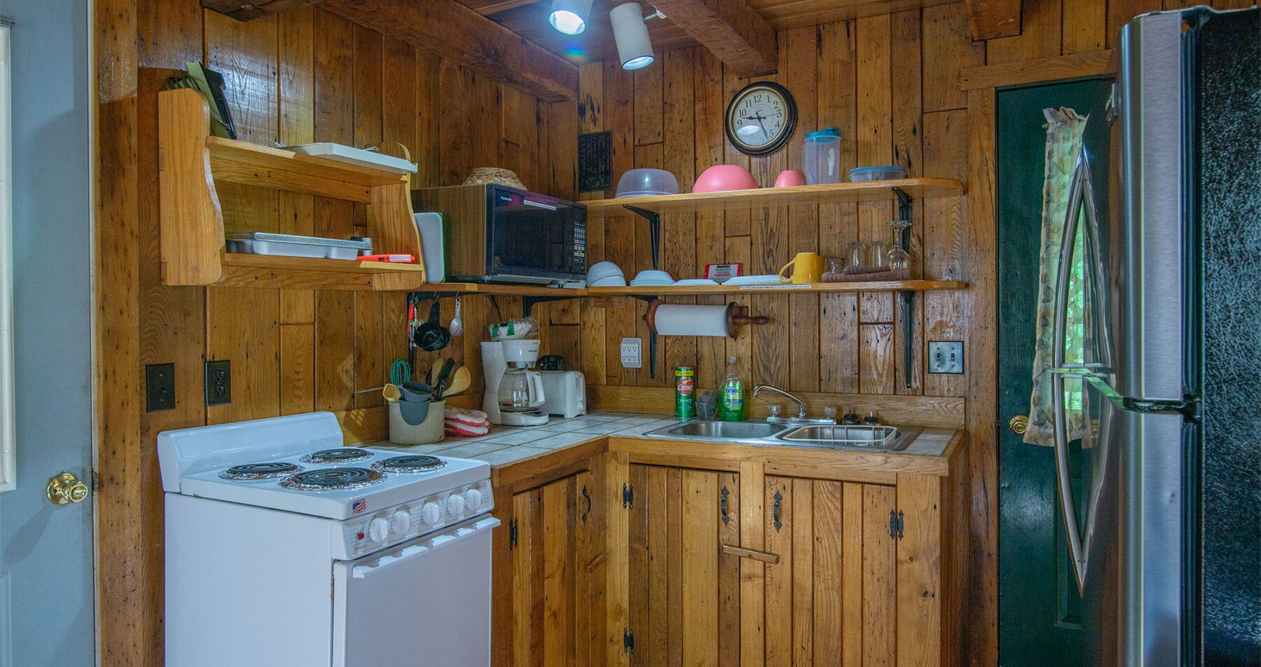 Une cuisine aux murs lambrés, équipée d’une cuisinière, d’un four à micro-ondes, d’un évier et d’un réfrigérateur.