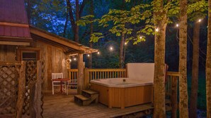 A wooden deck with a hot tub, a chair, and a small table. - Moore House Inn & Cabins (Marlinton)