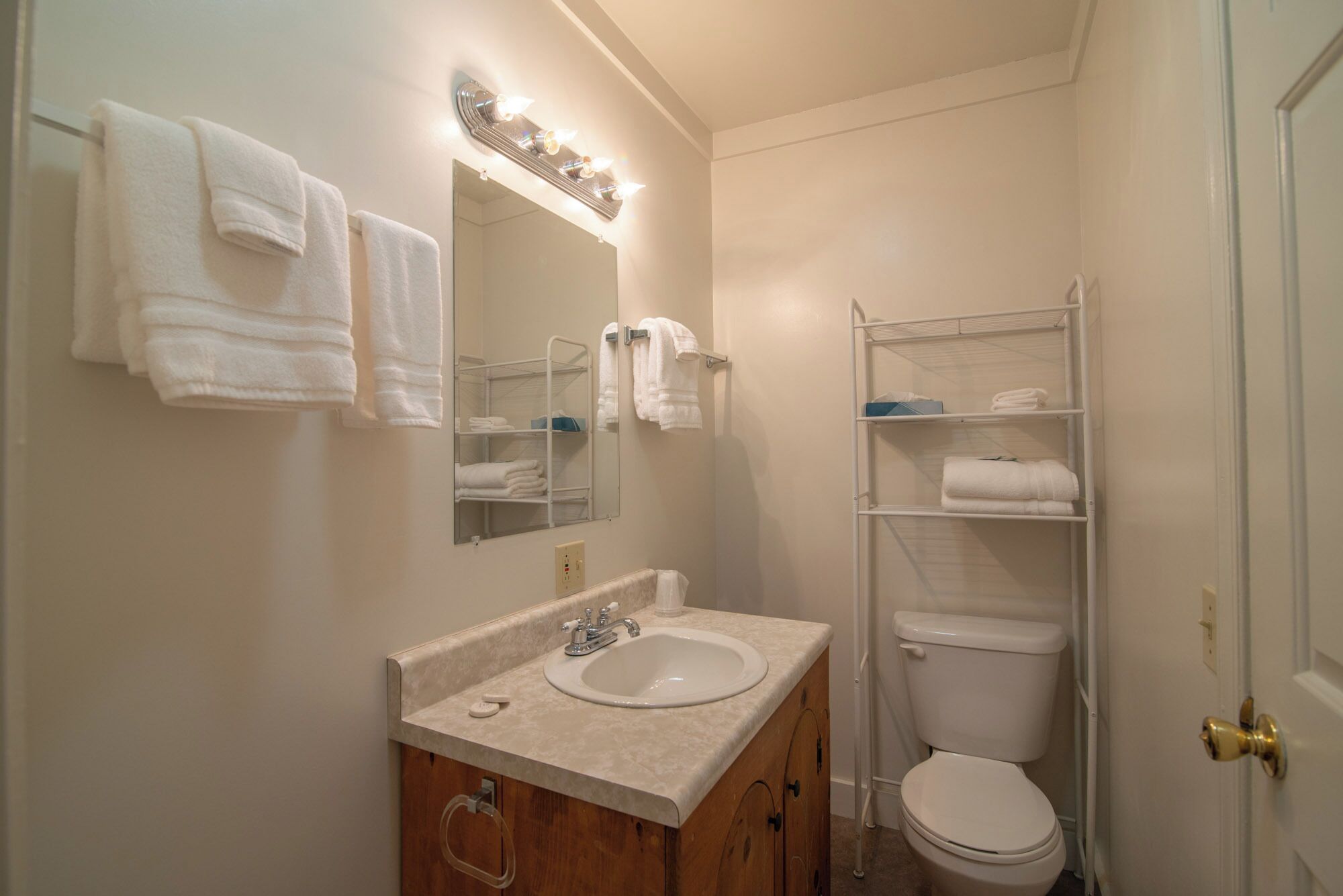 Een badkamer met een wastafel, spiegel en toilet. Handdoeken hangen aan de muur en er zijn planken met handdoeken en toiletartikelen.